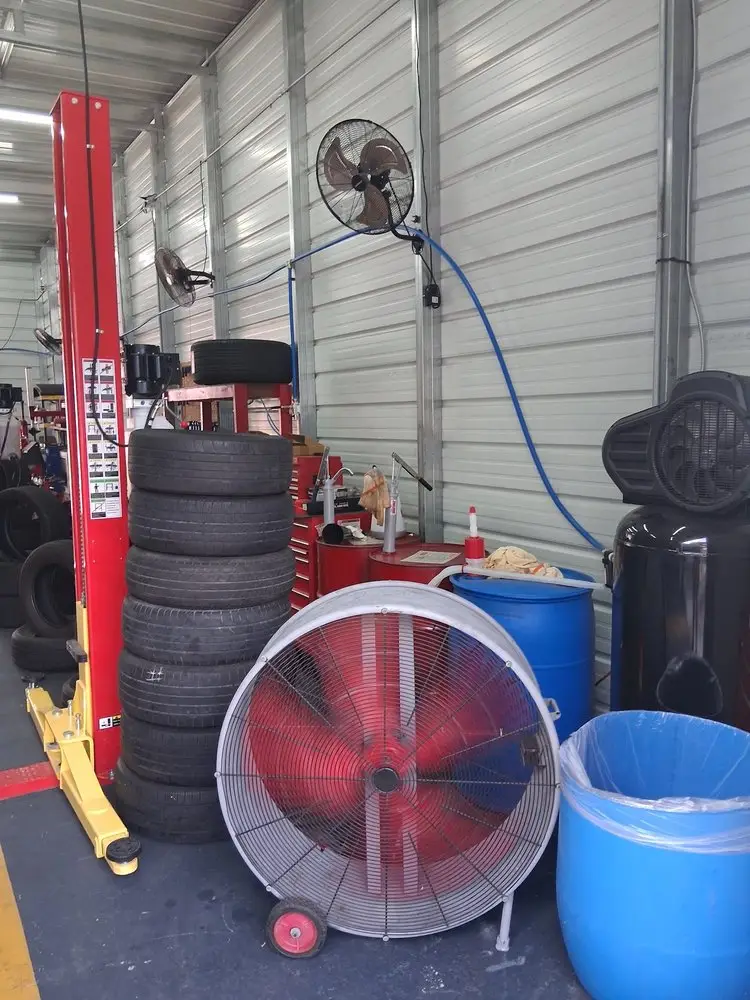 Red two-post car lift, stacked used tires and a large shop fan inside the service bay