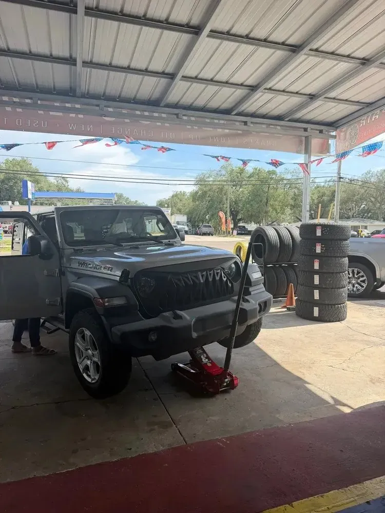 Gray Jeep raised on a floor jack for tire work under the shop's covered bay