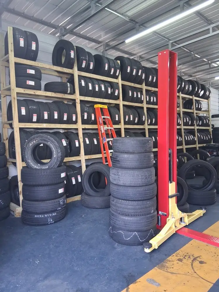 Wooden racks full of new and used tires beside a red car lift inside the shop