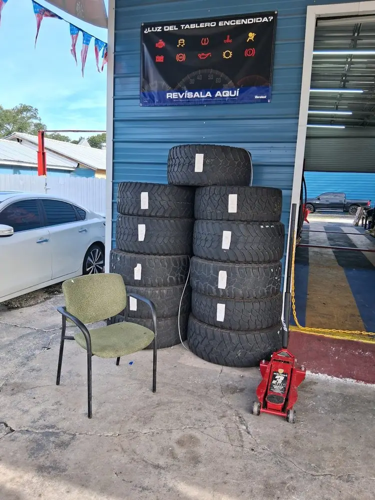 Stack of large used truck tires and a floor jack beside the shop's open bay door
