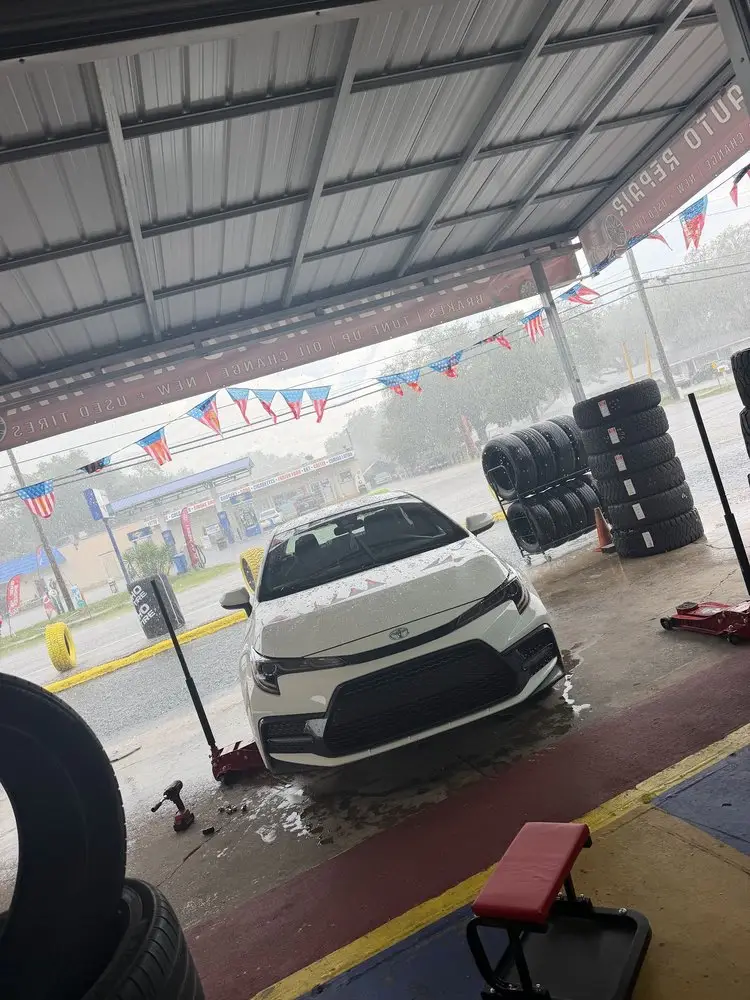 White sedan raised on a floor jack for new tires under the shop's covered bay